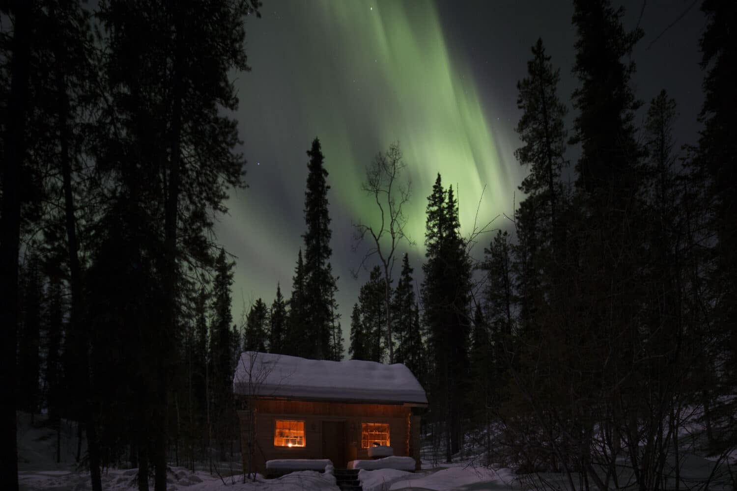 Cabin under vibrant northern lights.